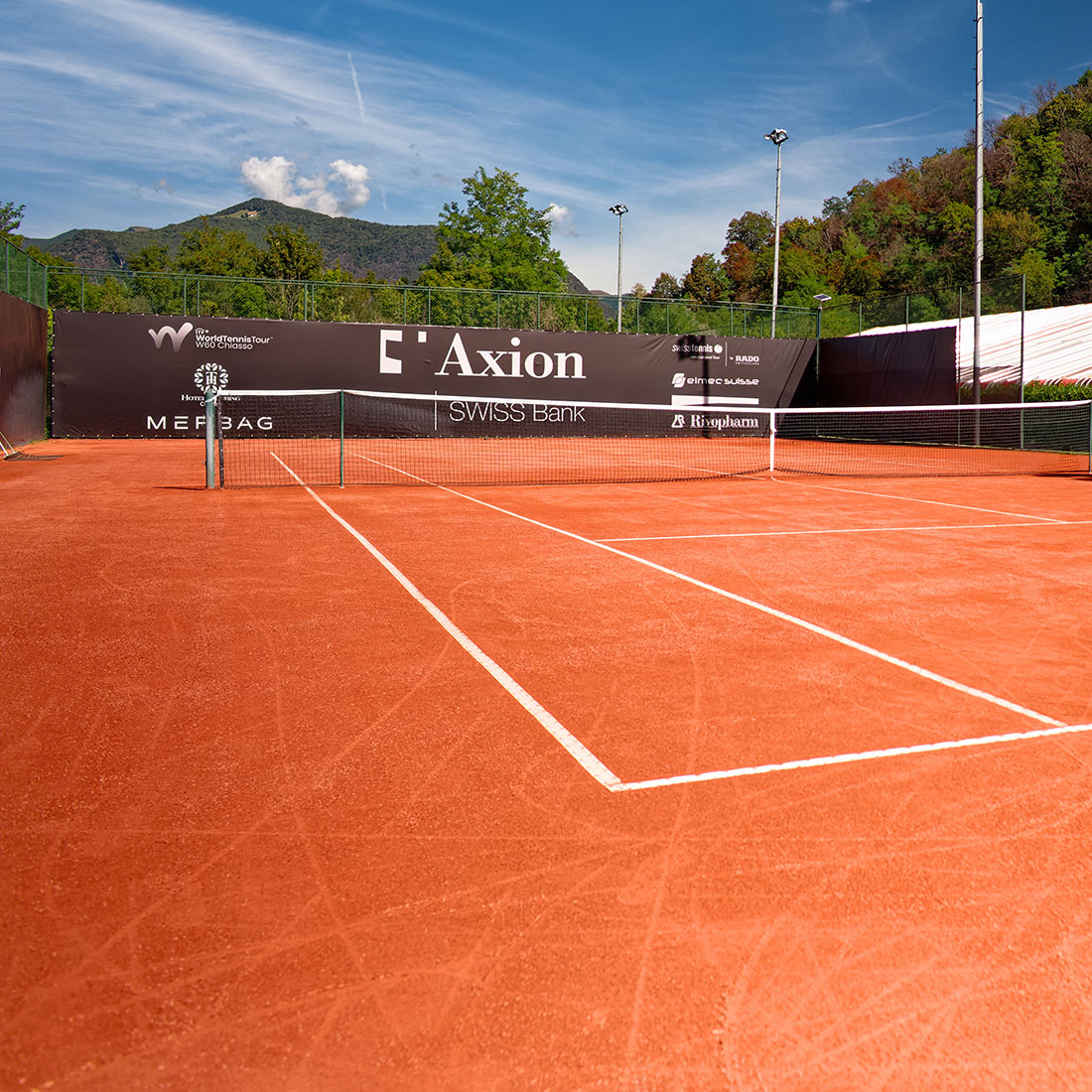 Rode gravelbaan van RedPlus met het net in het midden en sponsoring van de World Tennis Tour