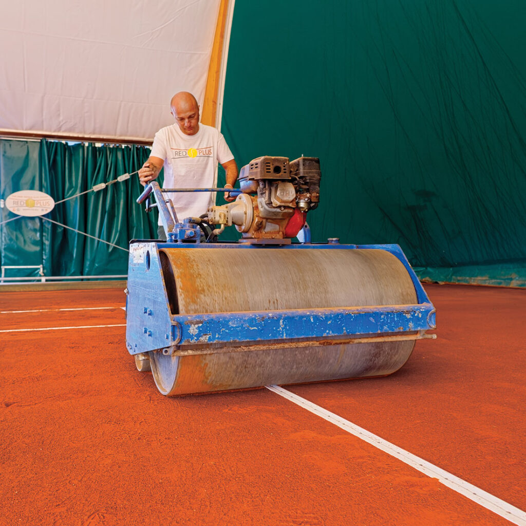 Medewerker van RedPlus met een professionele wals op een rode gravelbaan, voor onderhoud en verzorging van de ondergrond