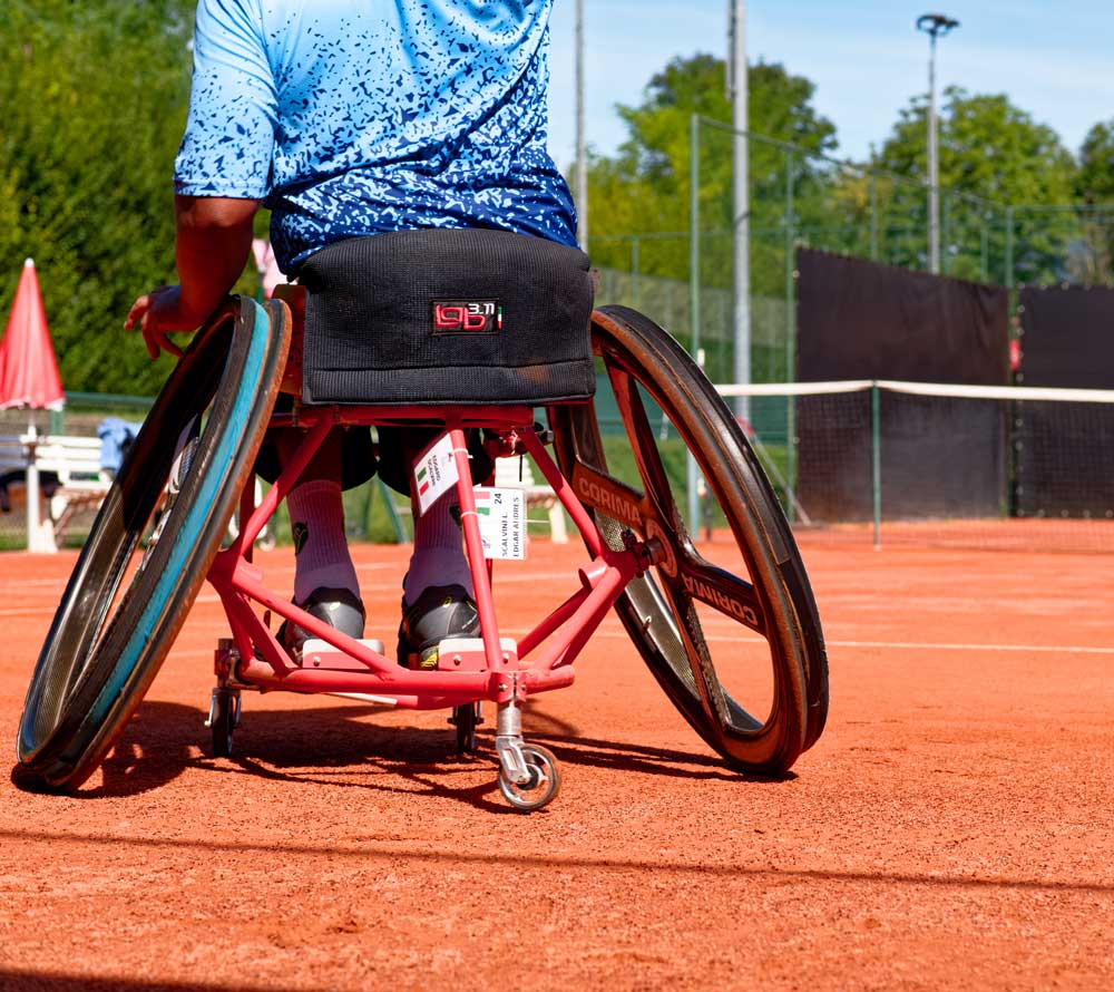 Rolstoeltennisser op een rode gravelbaan van RedPlus, de ideale ondergrond voor inclusief tennis.